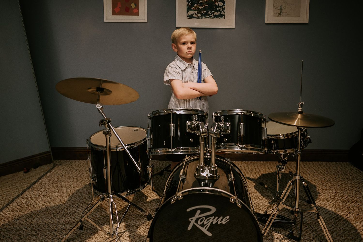 Young drummer sits behind a black Fame drum kit in a studio room with framed artwork on the wall.