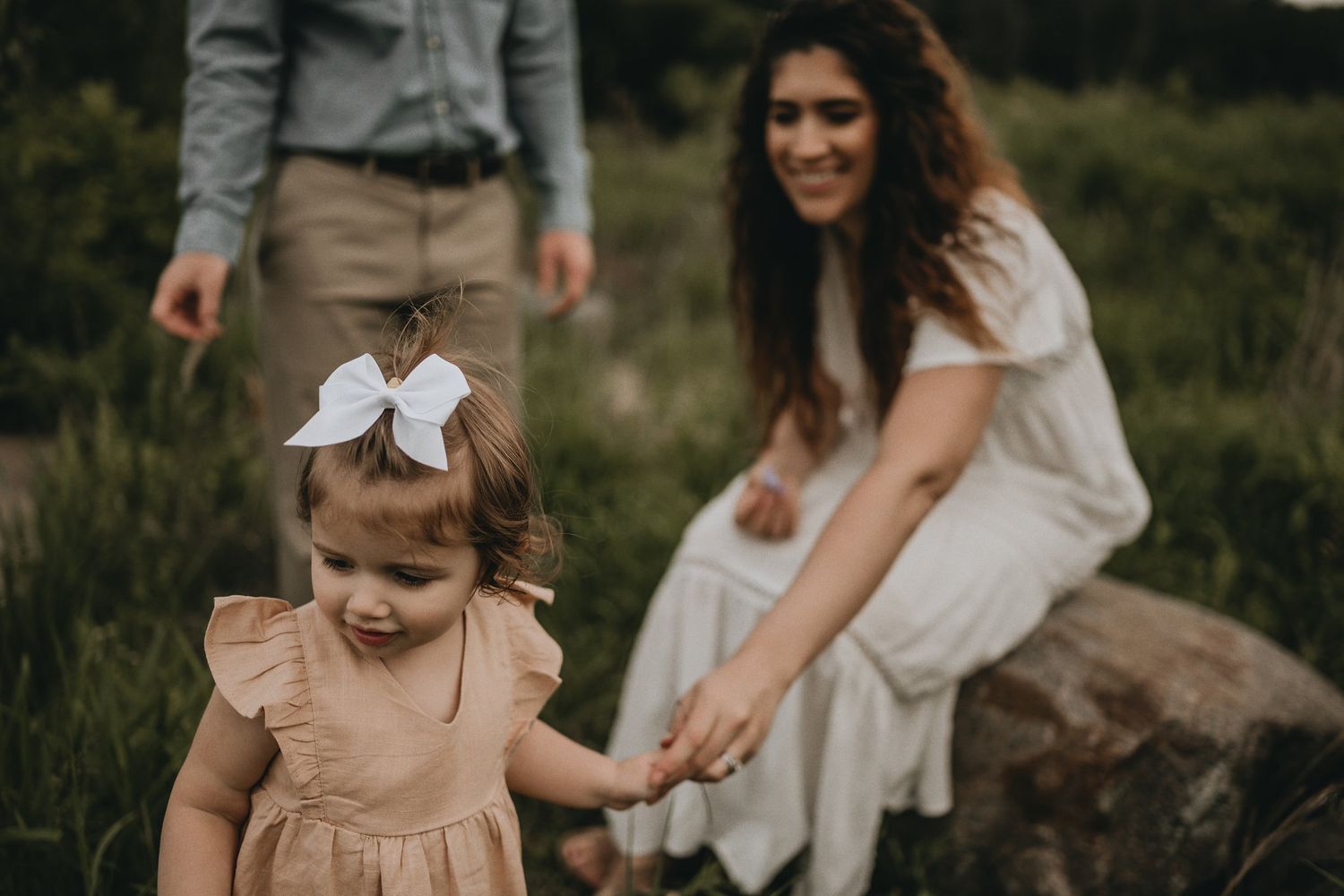 A playful outdoor scene with a small child in a peach dress and bow exploring nature.