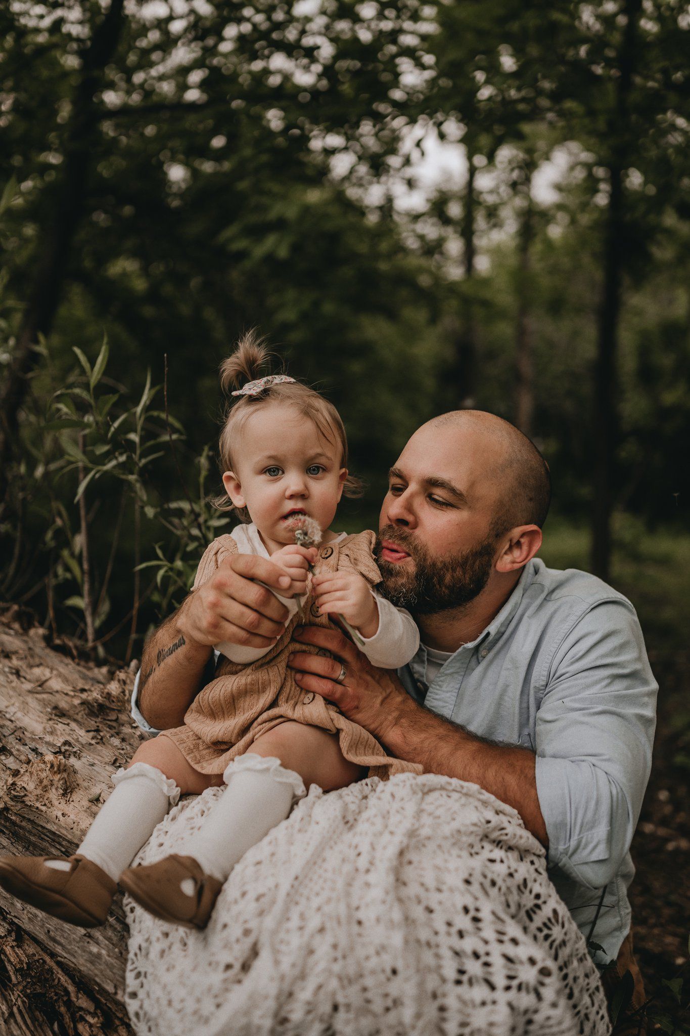 An intimate moment between parent and child sitting on a fallen tree in the woods.