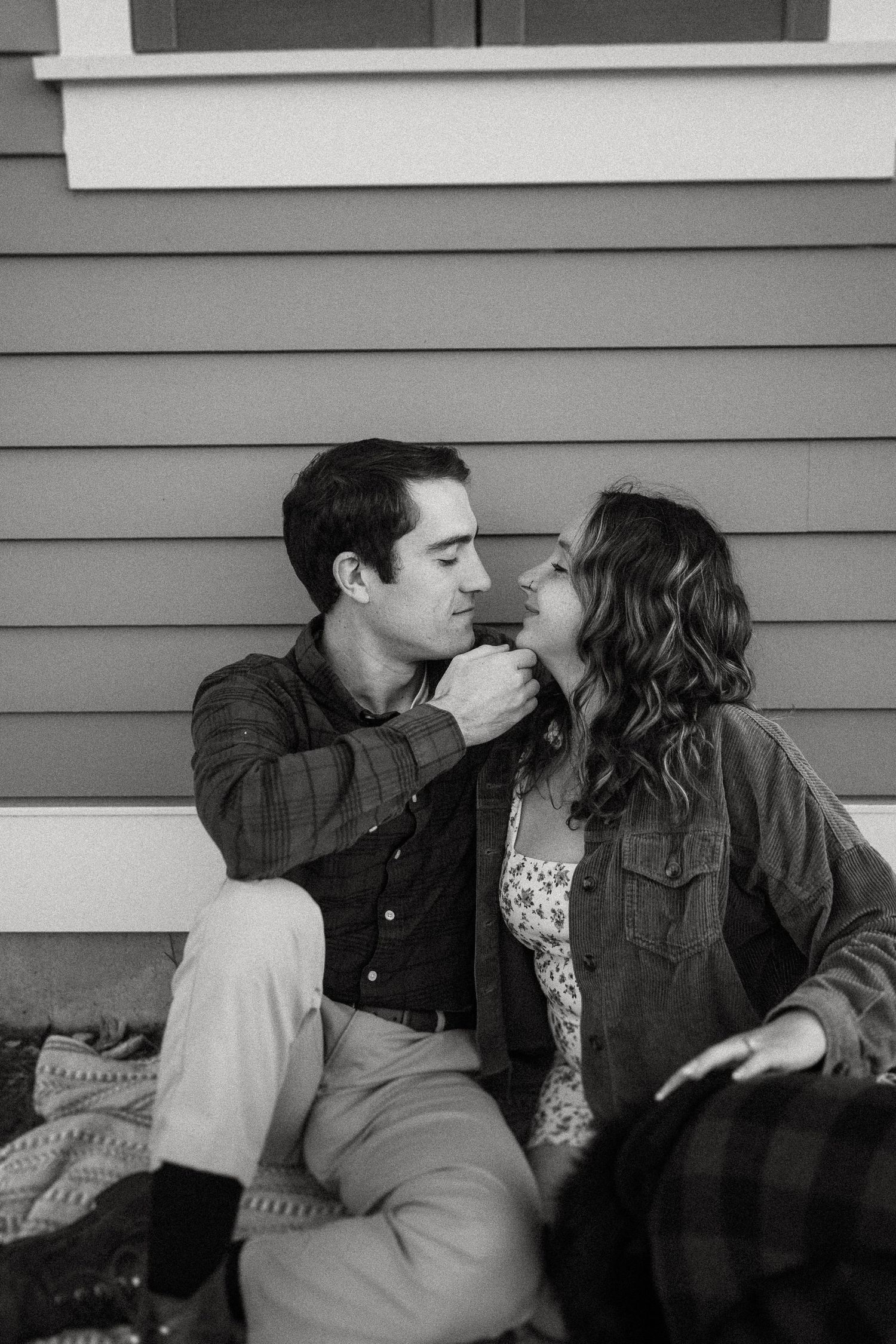 Intimate black and white portrait of couple sitting against house exterior.