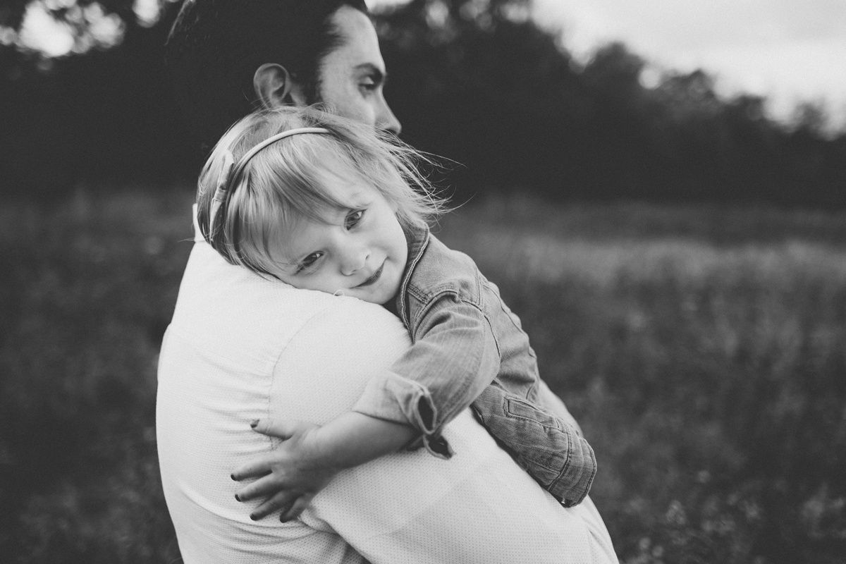 Black and white candid shot showing tender embrace between parent and child in a field.