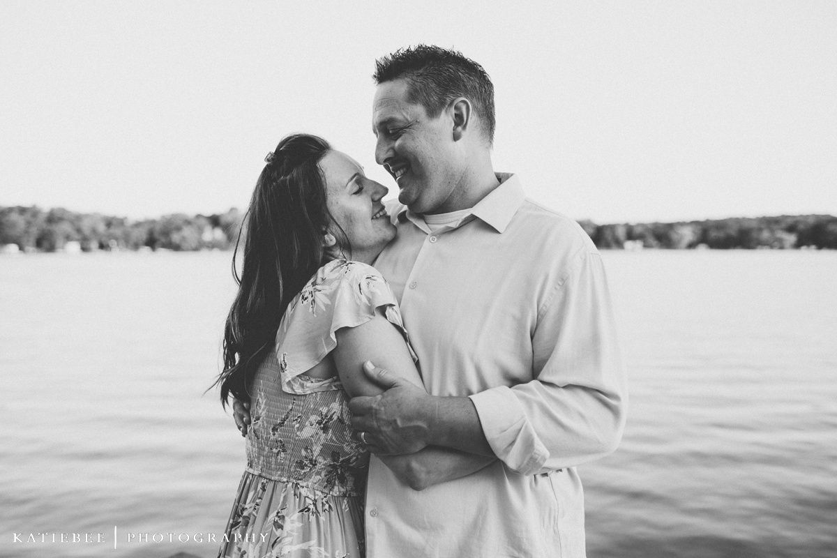 Black and white portrait of couple embracing by lake during intimate photoshoot.