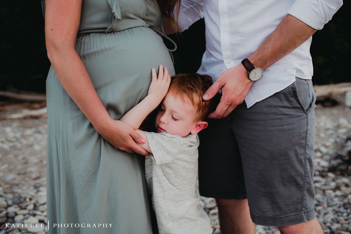 Tender family moment captured on a rocky beach with gentle waves in the background.