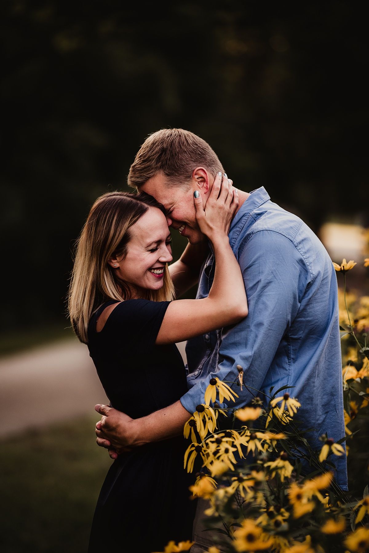 Romantic couple embracing and laughing among yellow flowers in garden setting.