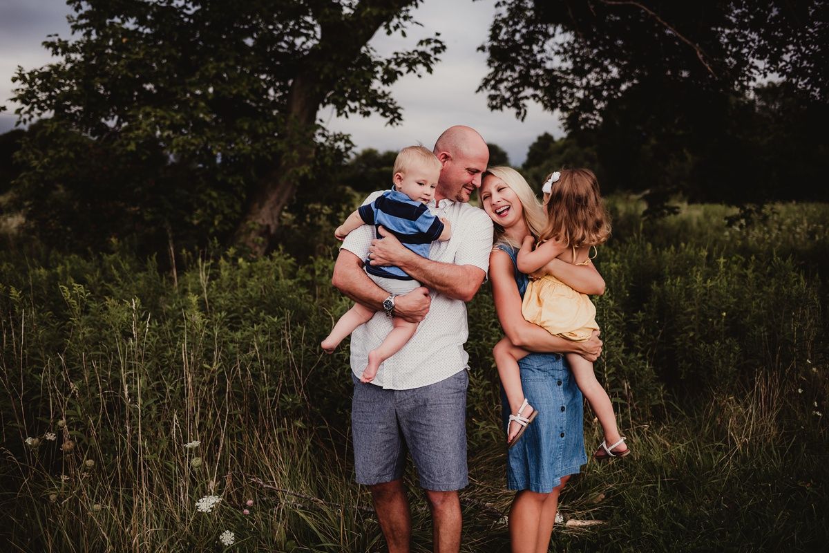 Intimate family portrait in golden hour light among wildflowers and trees.