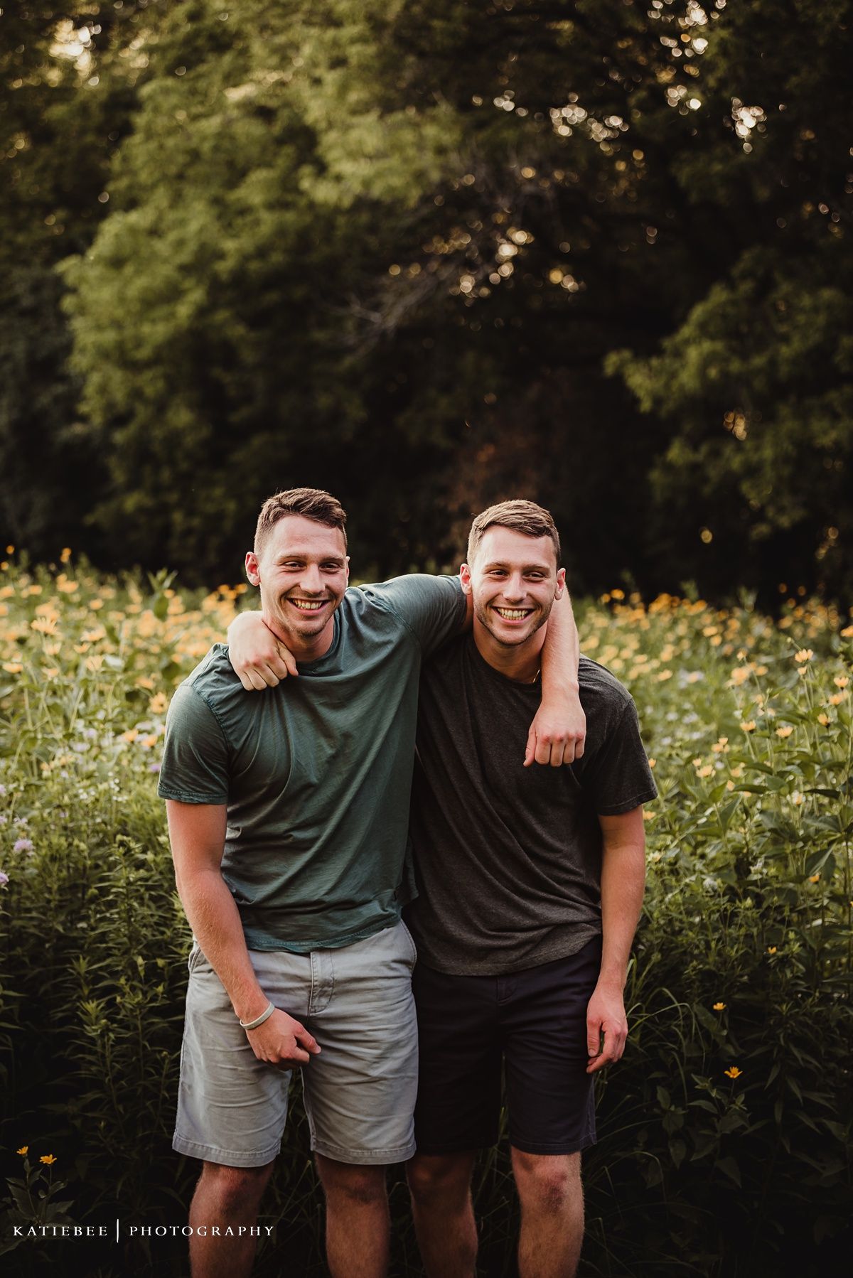 Two people share a friendly embrace while standing in a field of yellow wildflowers at sunset.
