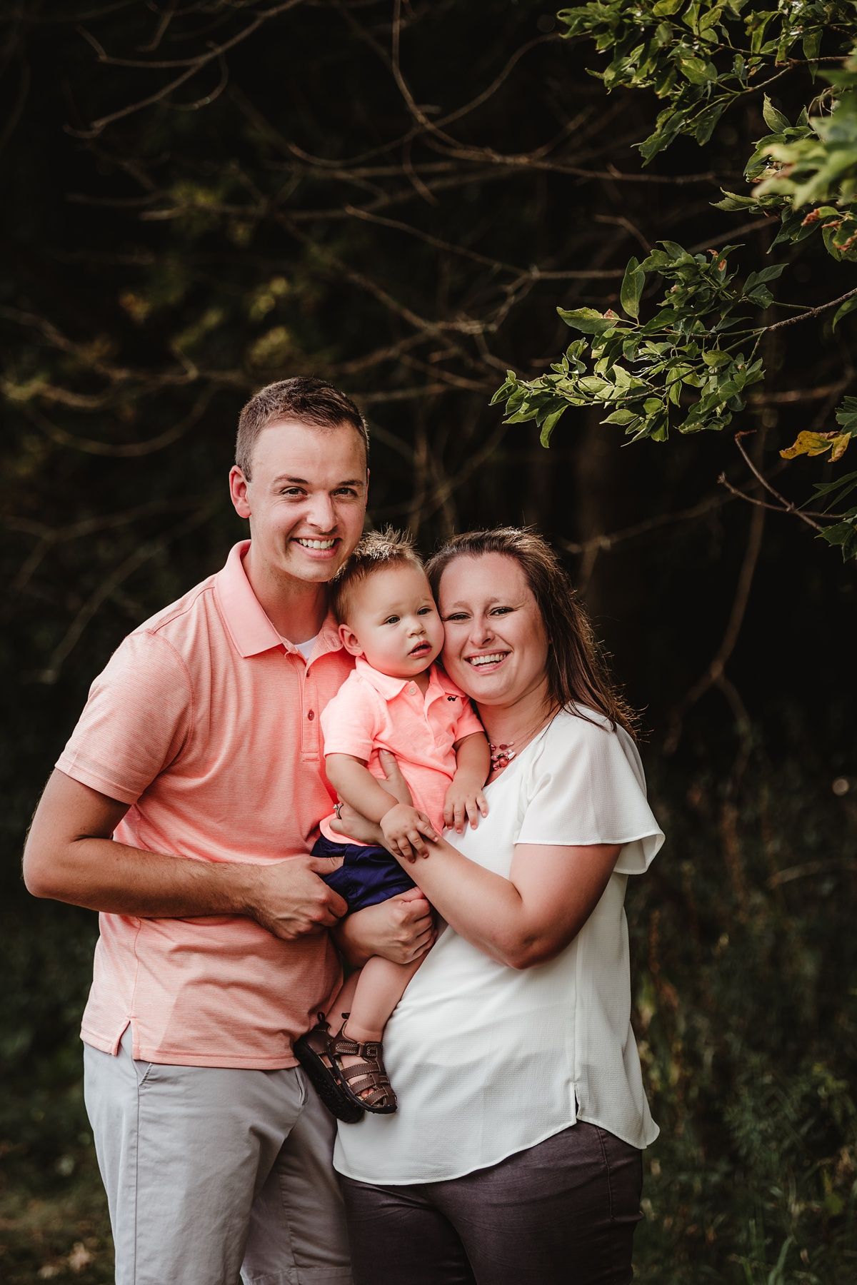 Family portrait in coordinating coral and white outfits against dark foliage background.