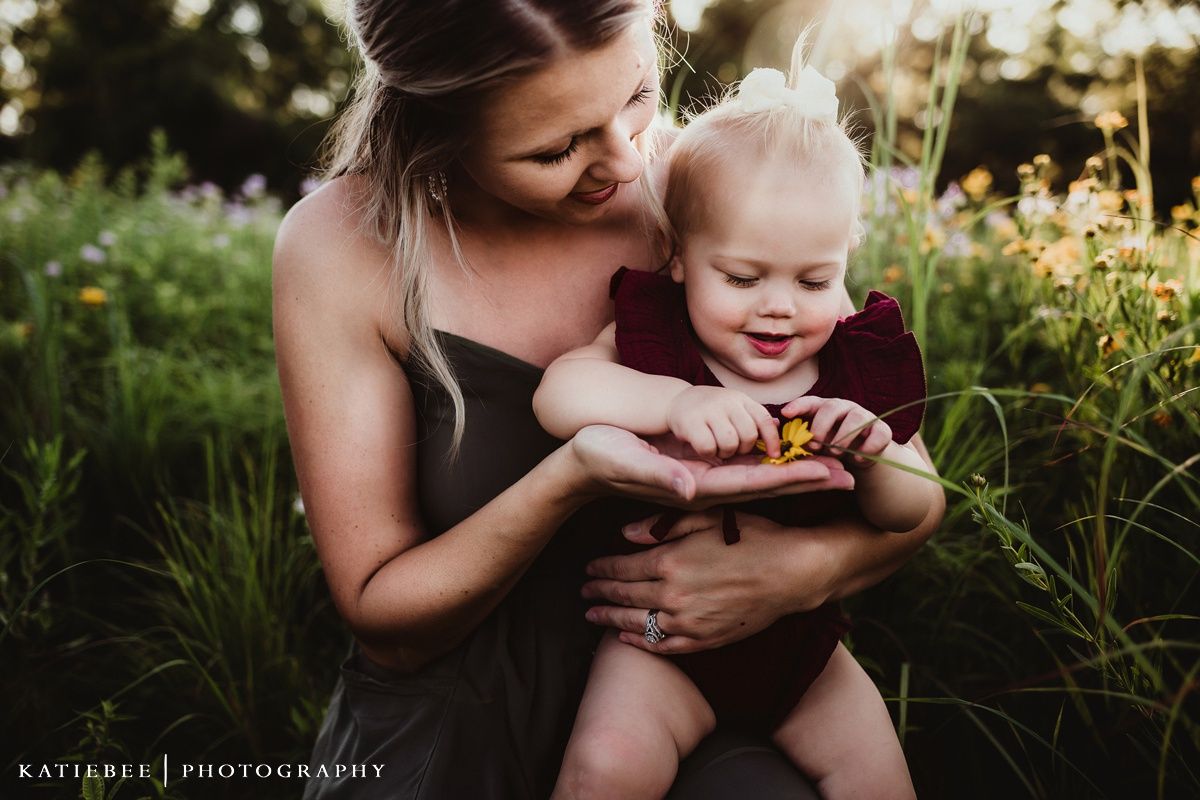 A tender outdoor moment captured in golden light as parent and child share a laugh among wildflowers.