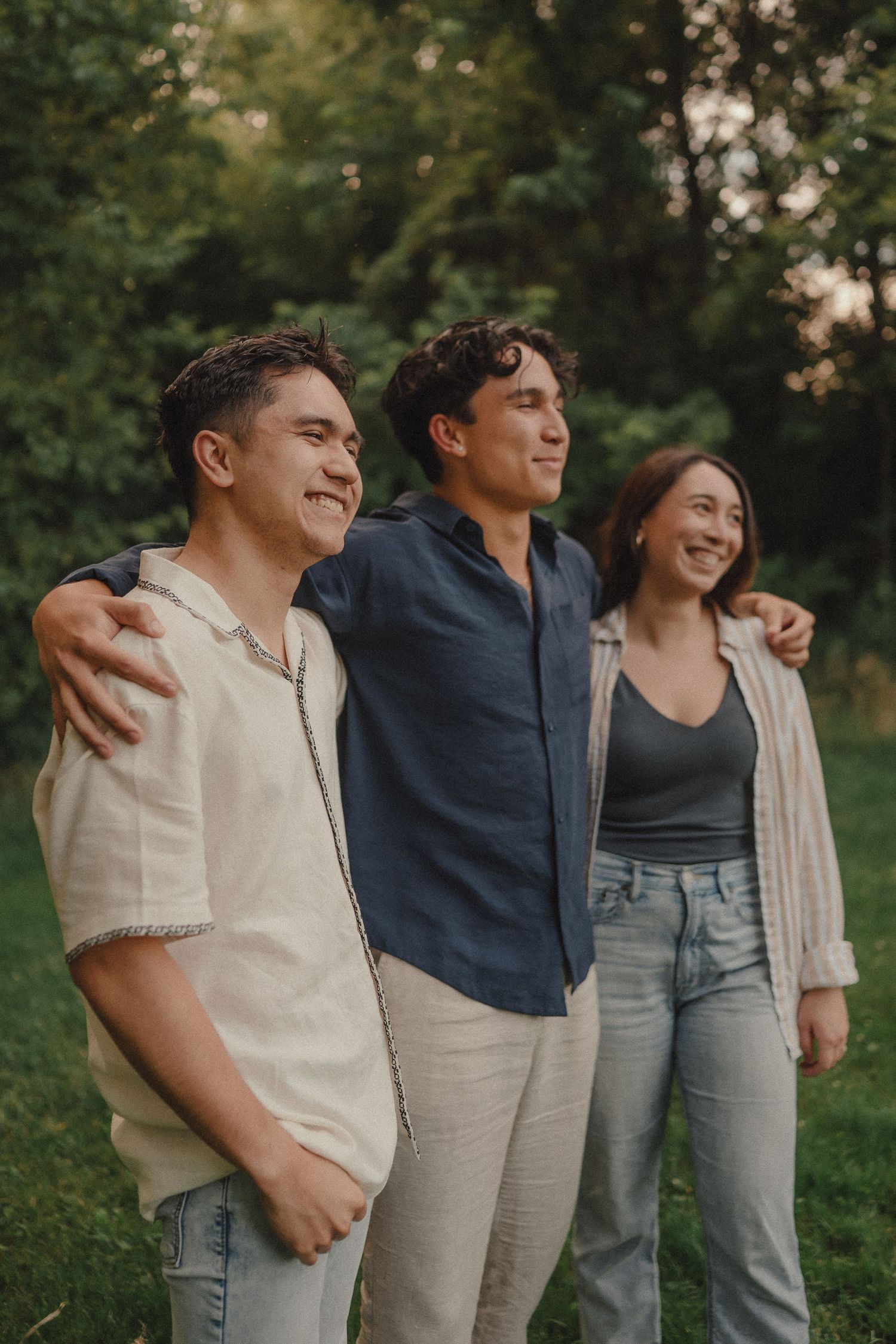 Three young adults smiling and posing together outdoors in a lush green park setting.