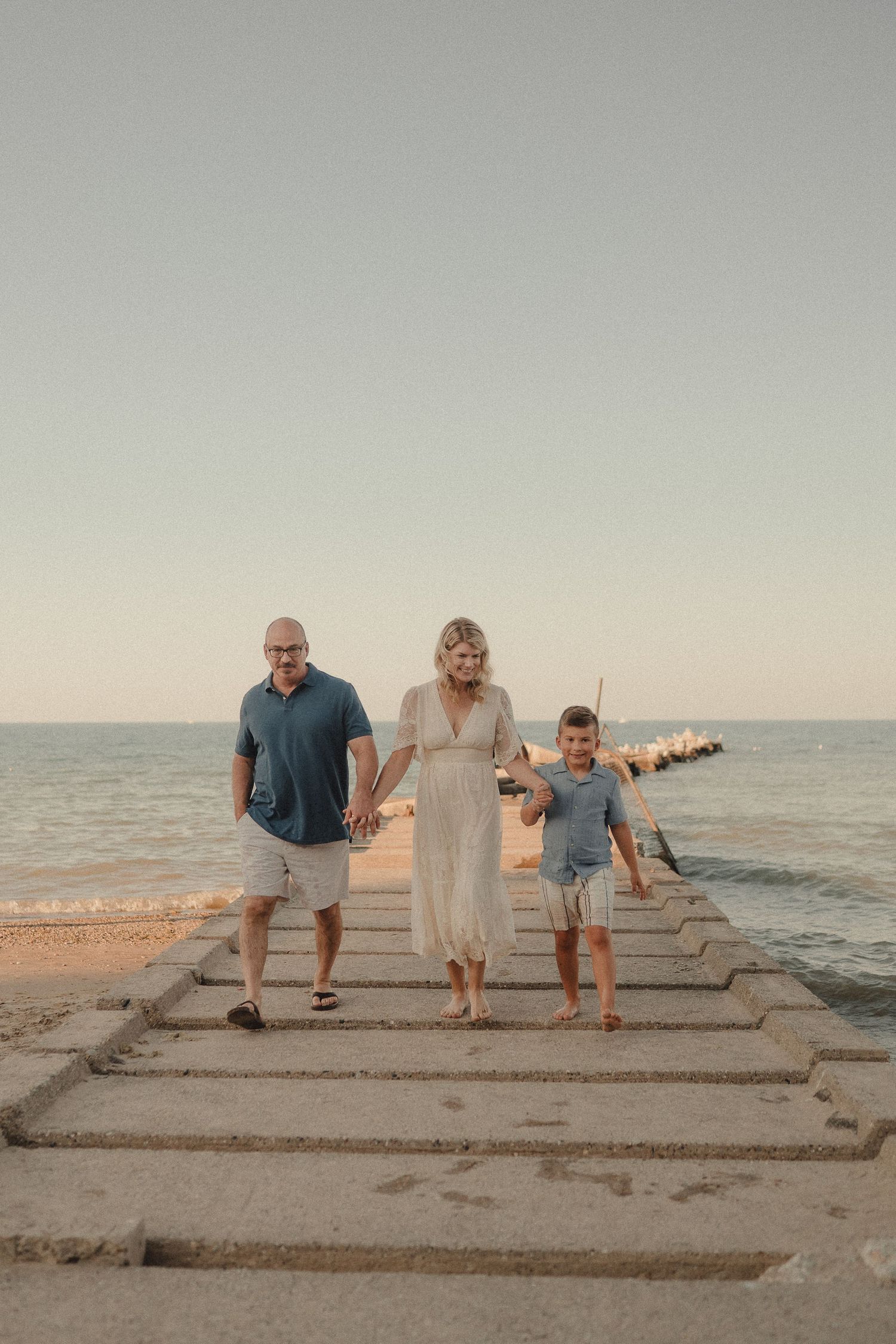 Family of three walking together on a concrete pier with the ocean in the background.