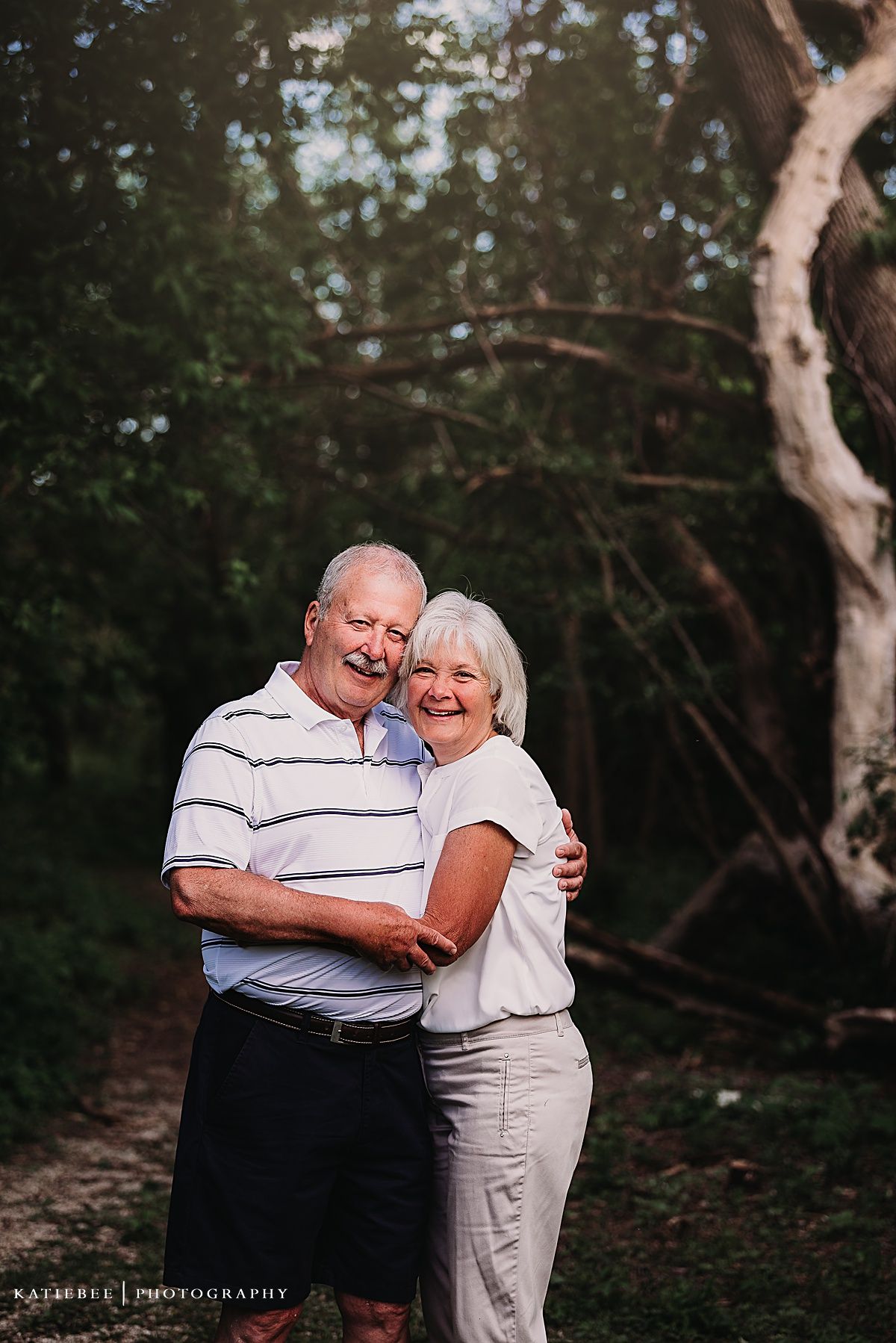 Senior couple embracing and smiling together on a wooded path.