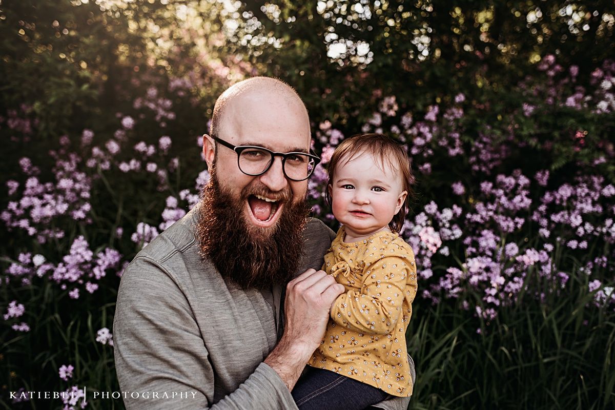 Joyful interaction between parent and child with purple flowers blooming in background.