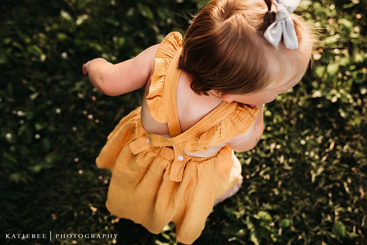 Close-up of mustard yellow dress with ruffles against green foliage background.