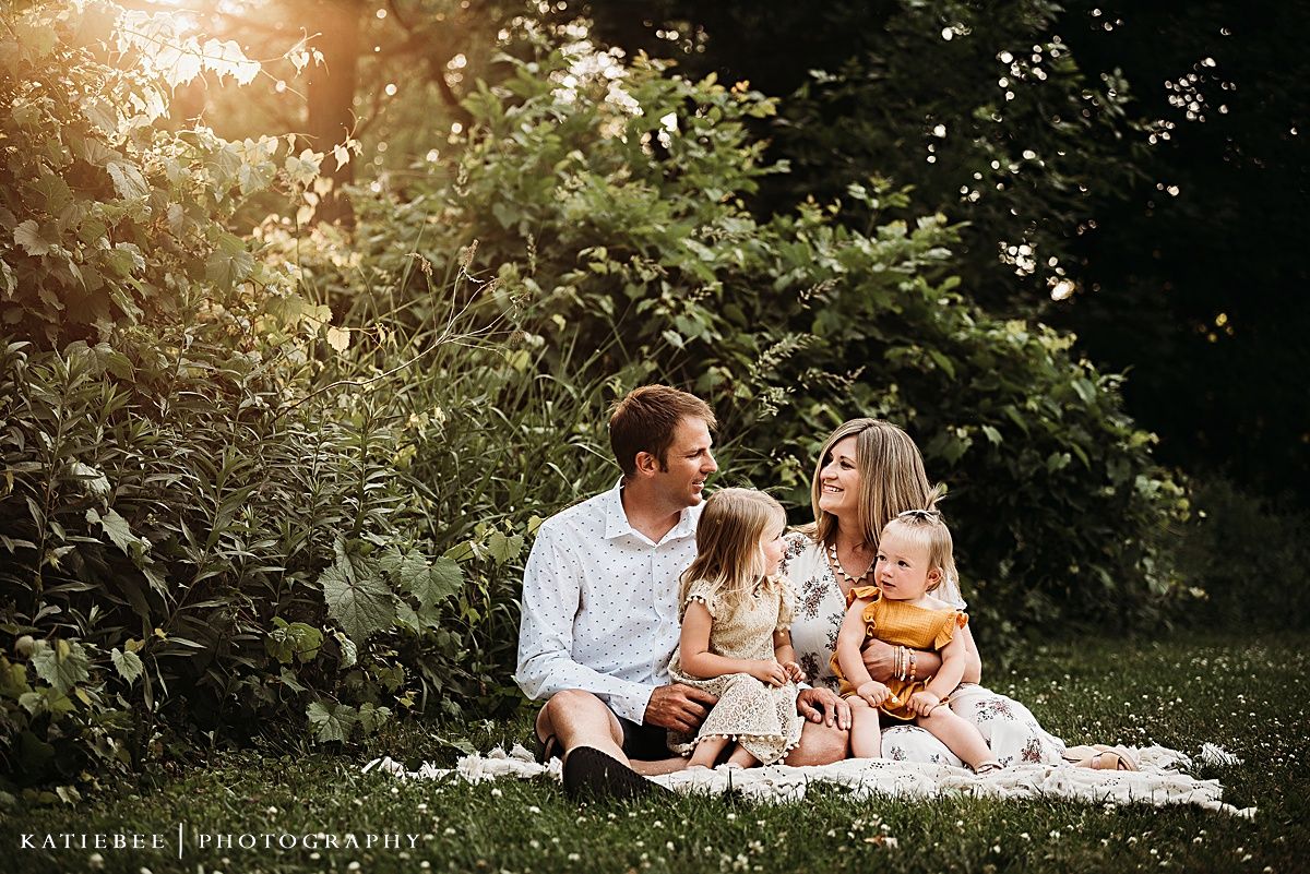 Family sitting together on blanket in garden during golden sunset.