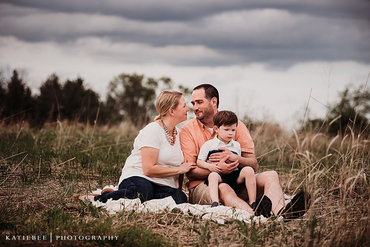 An intimate family portrait captured in a rustic outdoor setting with dramatic clouds above.