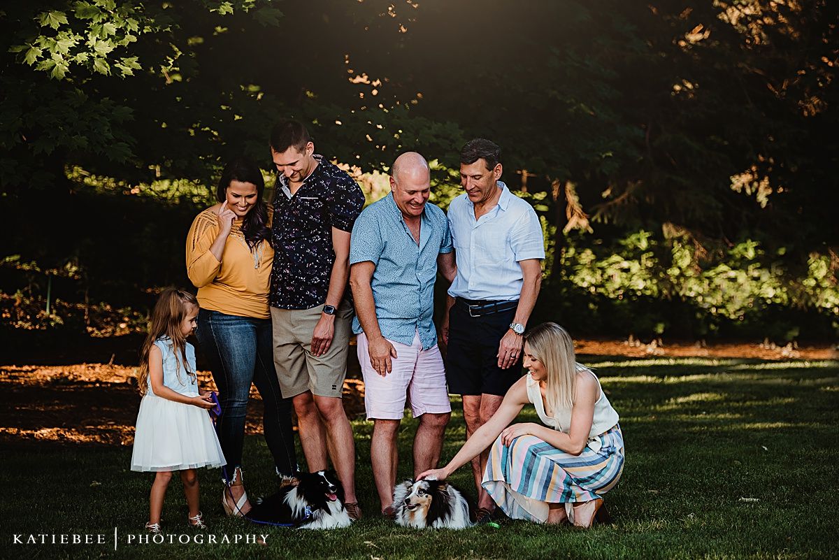 Family gathering outdoors with their dog in a sunlit park setting.