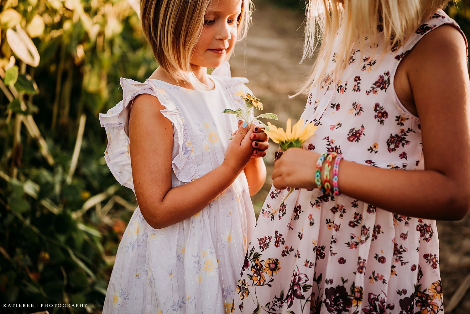 Close-up of children examining sunflowers together while wearing white and floral dresses.