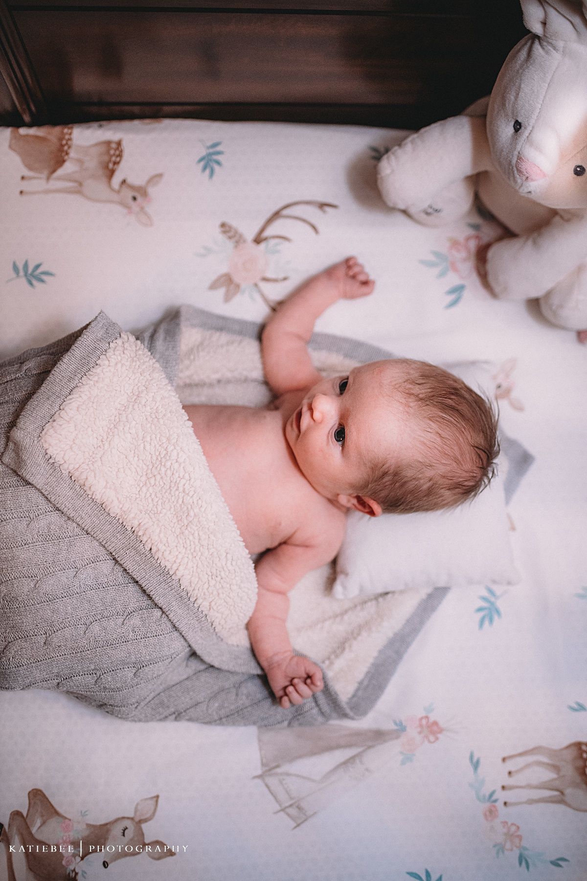 Sweet newborn photography of a baby lying on patterned bedding with stuffed animals.