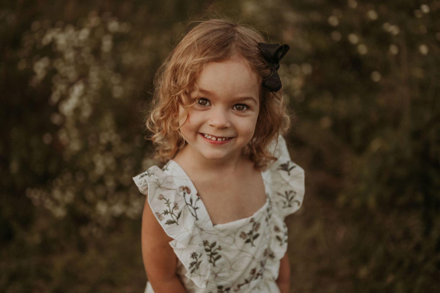 A whimsical portrait of a child in a floral dress with natural lighting outdoors.