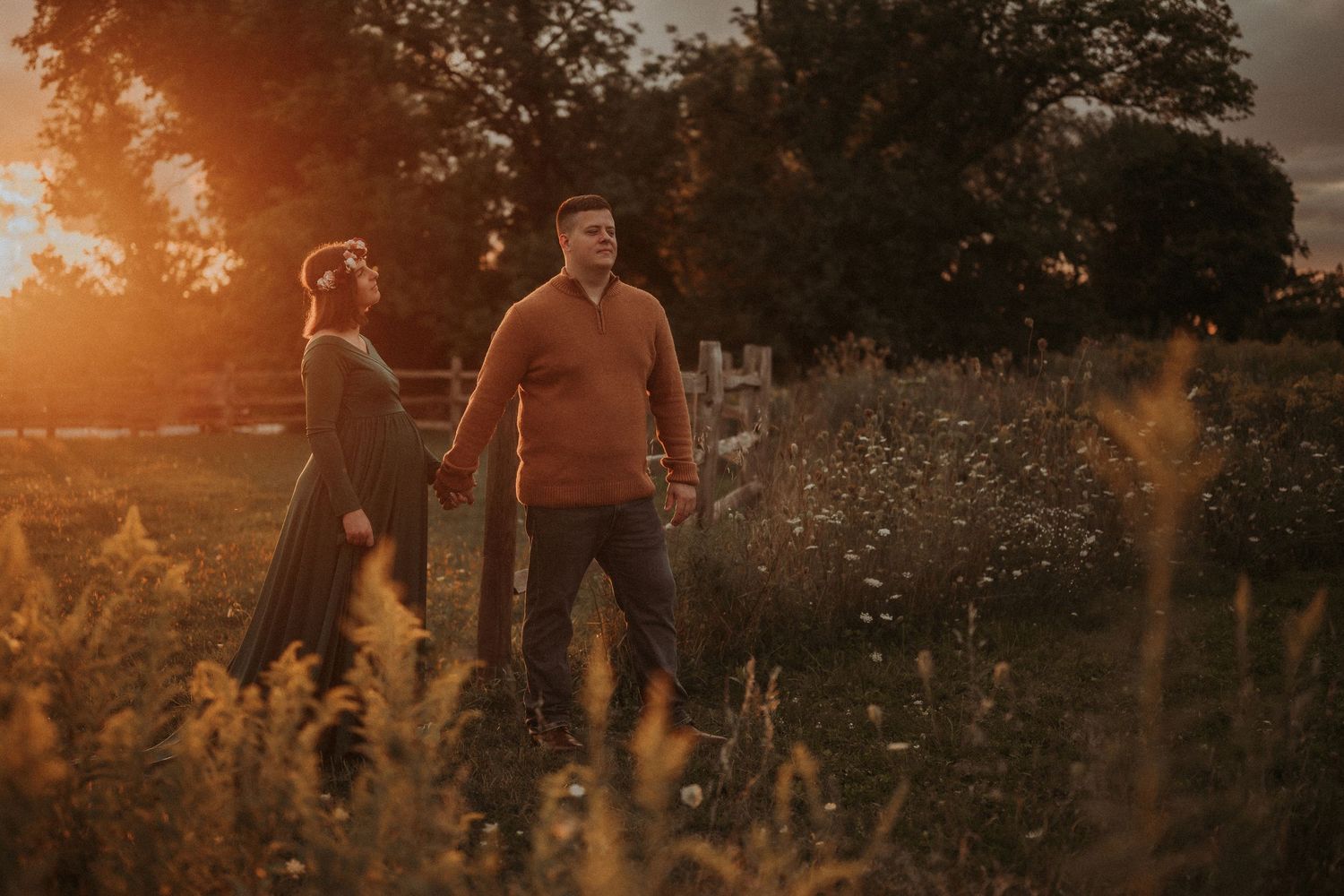 Couple walking through tall grass field during golden hour sunset.