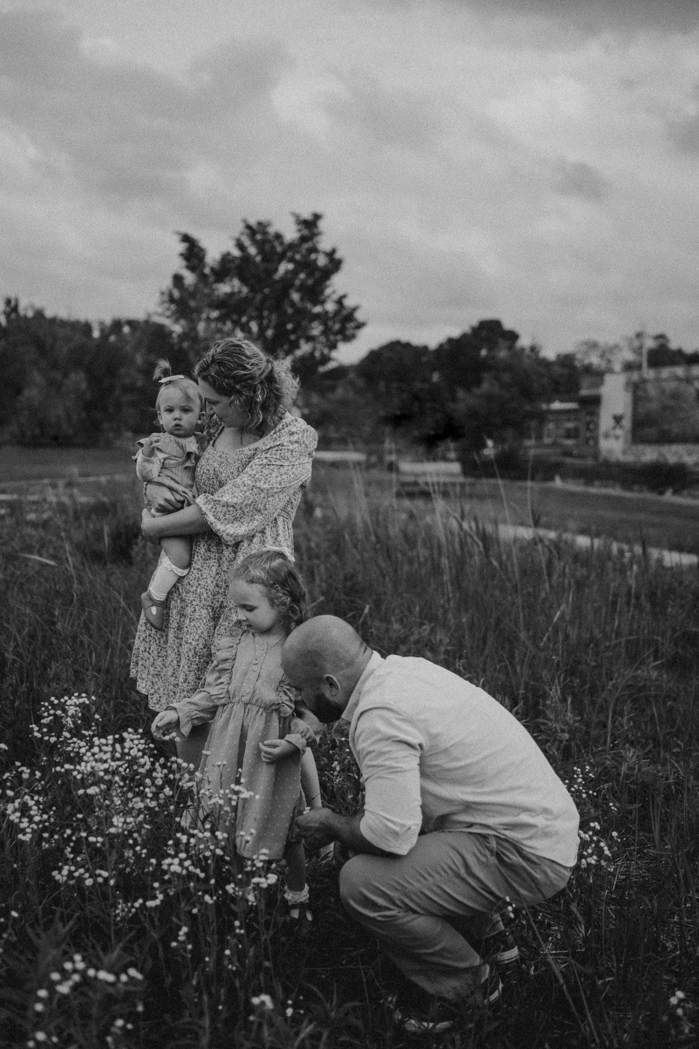 A candid black and white family portrait taken in a wildflower meadow at sunset.