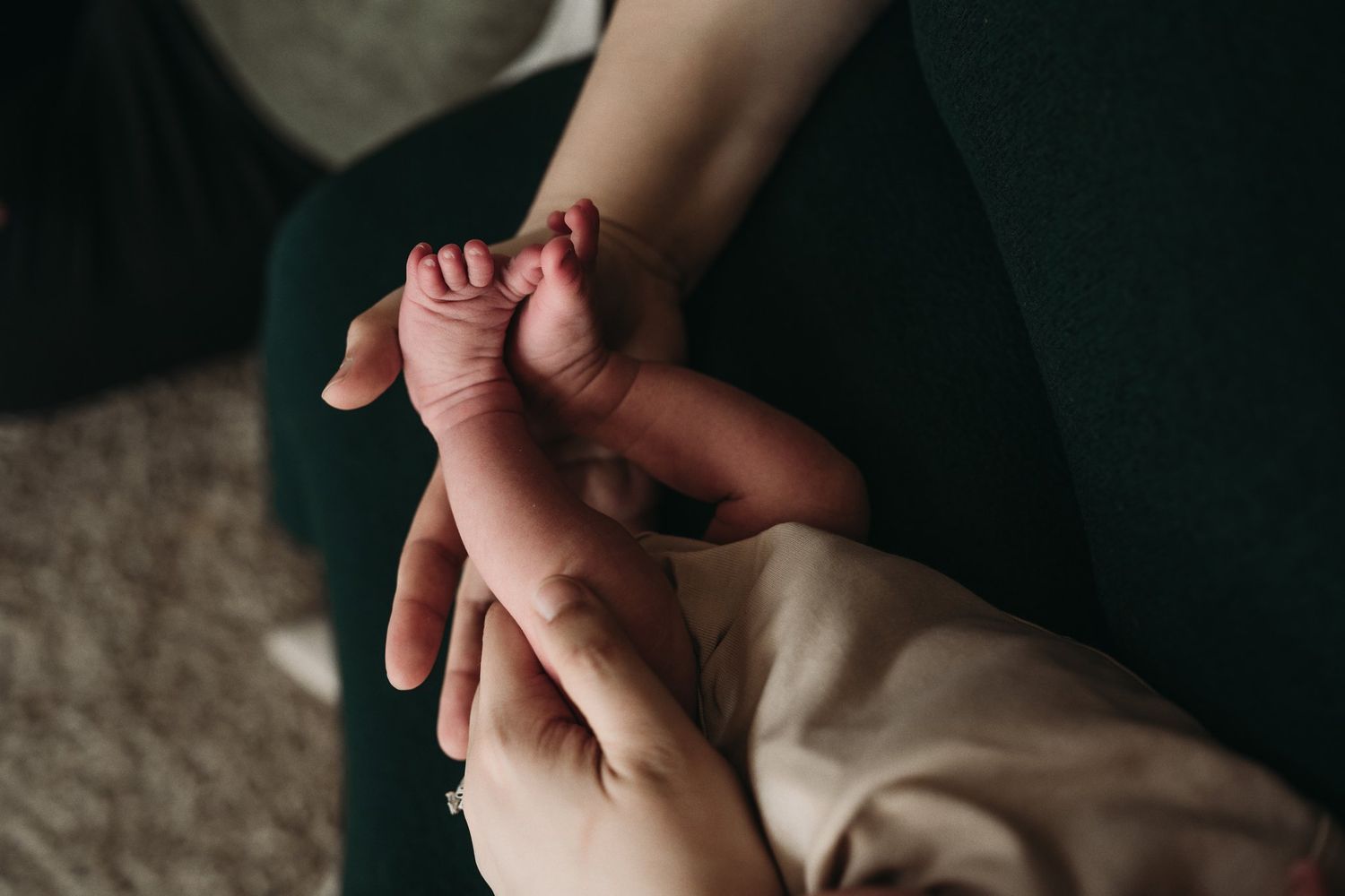 Close-up of tiny newborn feet being held by gentle hands on dark fabric.