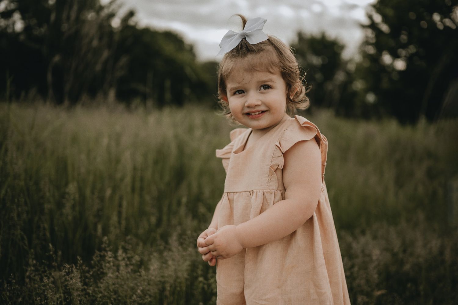 A sweet moment captured of a child in a peach-colored dress standing in a meadow.