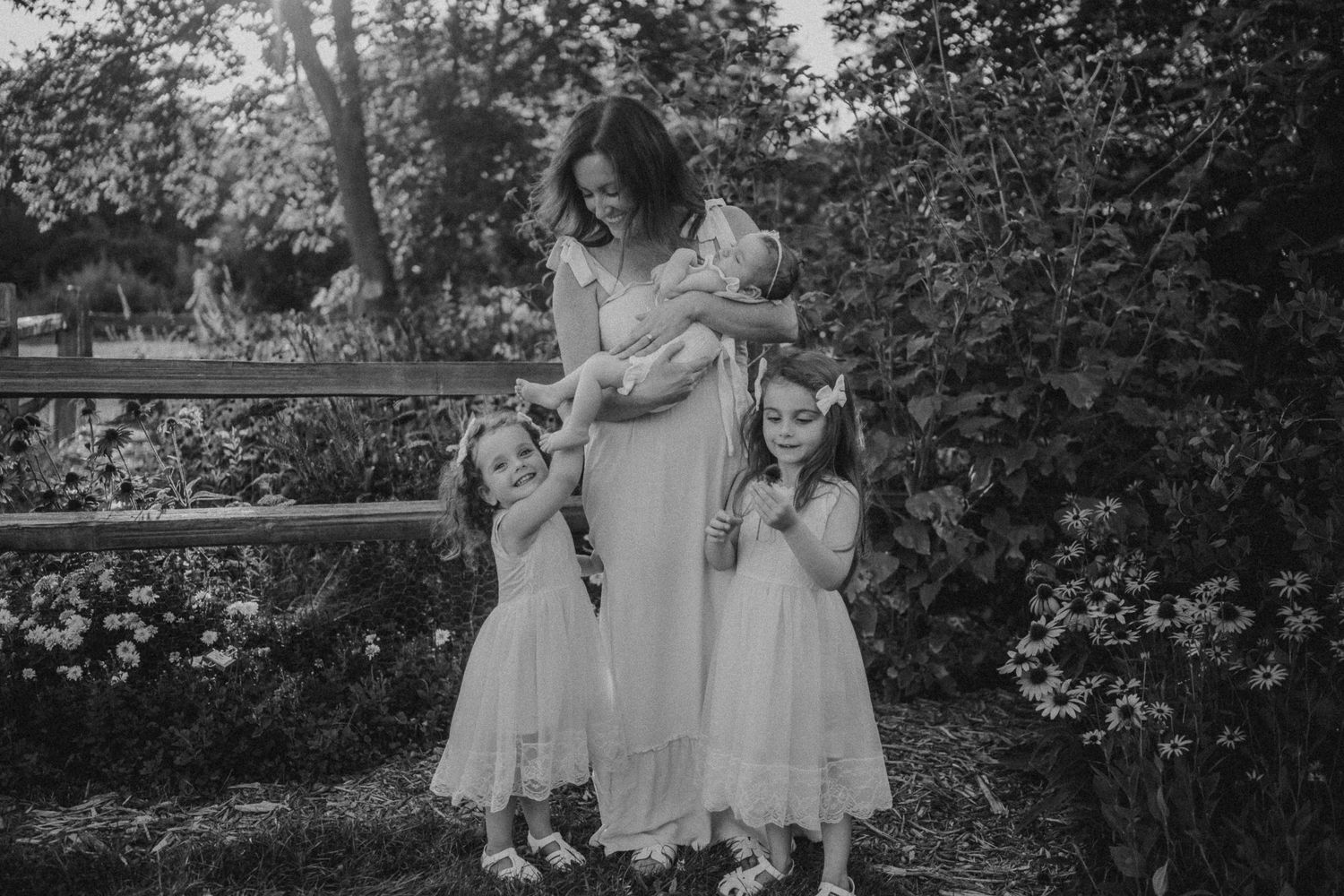 A black and white family portrait in a garden with delicate lace dresses and natural poses.