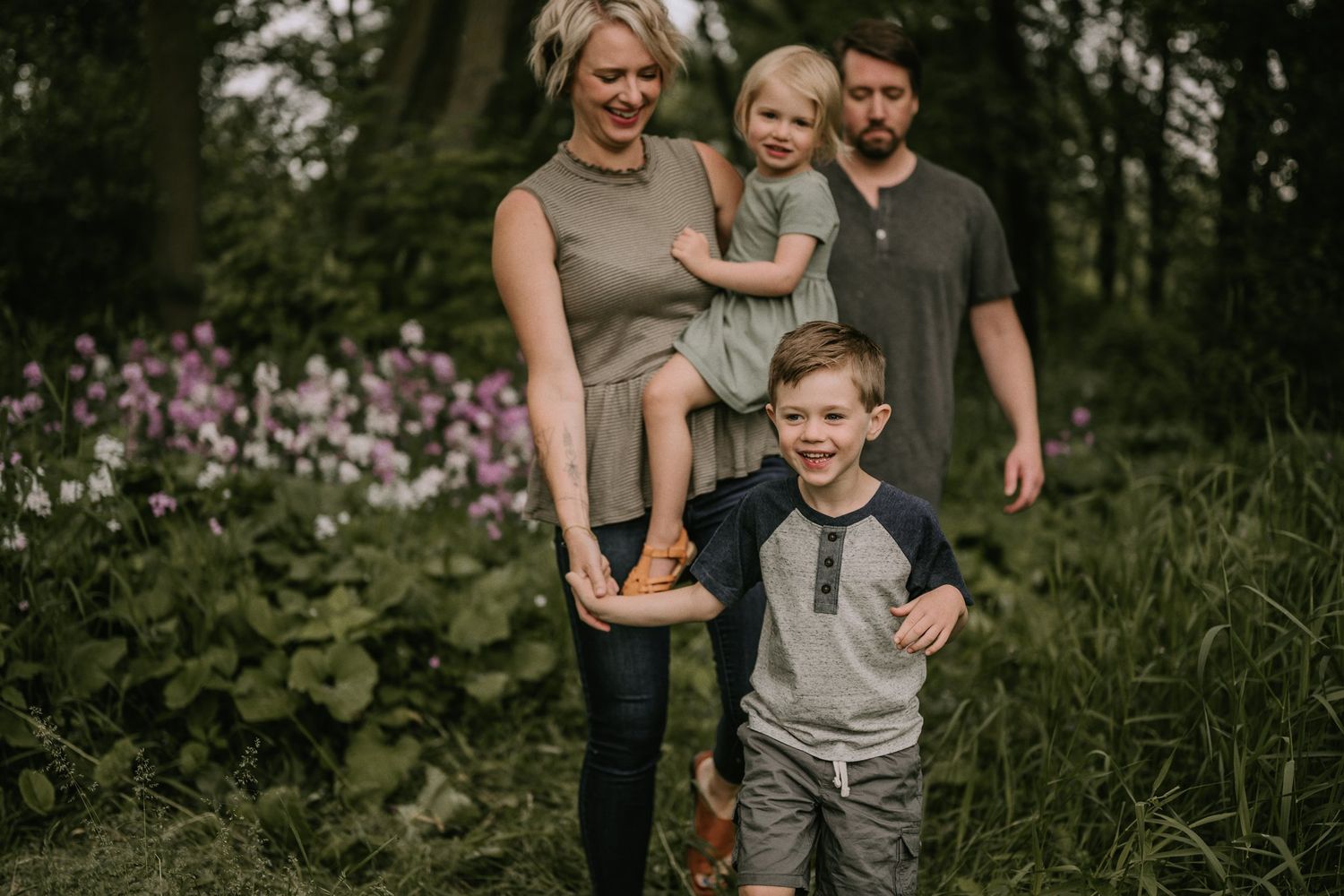 A family poses together in a garden with blooming pink flowers and lush greenery.