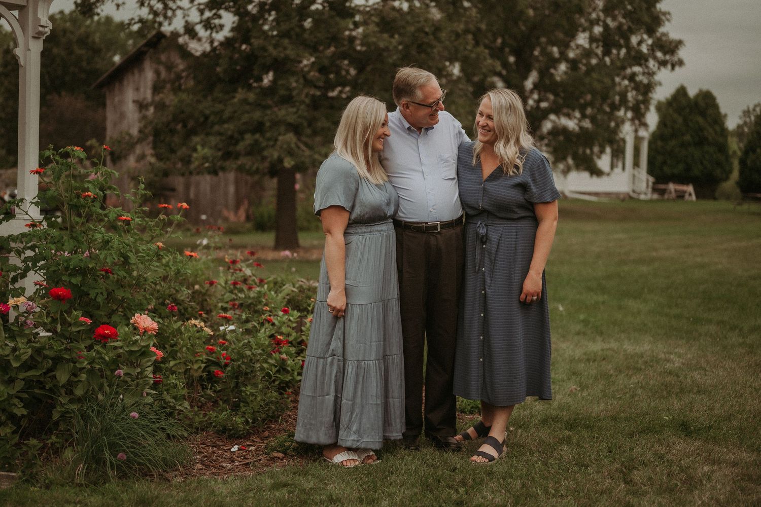 Three people share an intimate moment together in front of blooming rose bushes at sunset.