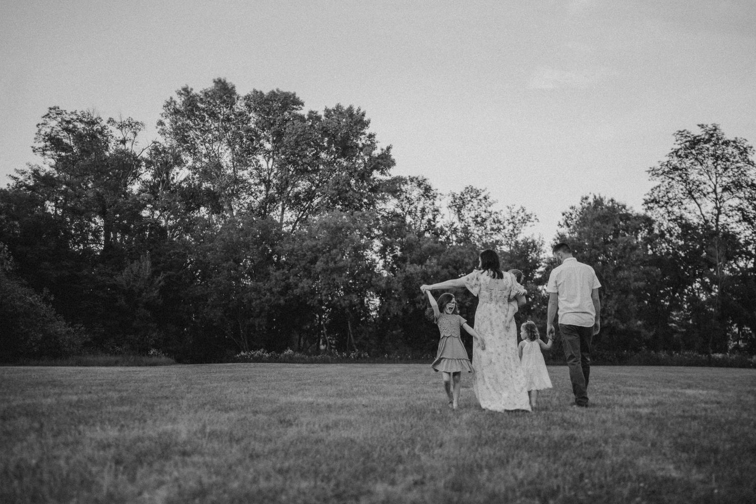 A black and white silhouette of a family walking together in a meadow at sunset.