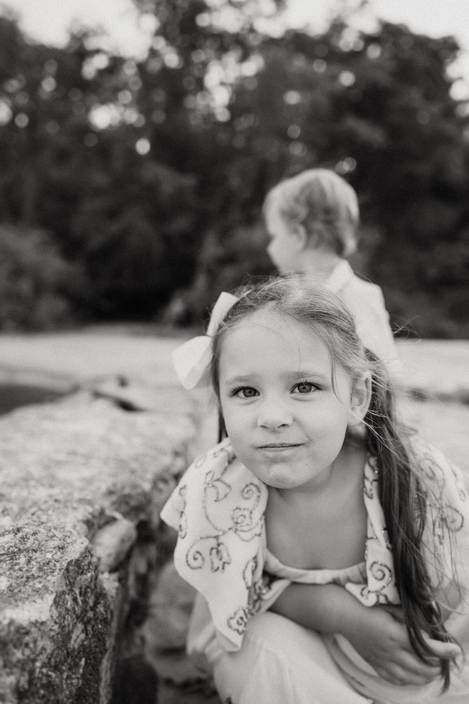 Two children relax on rocky coastal terrain in black and white.