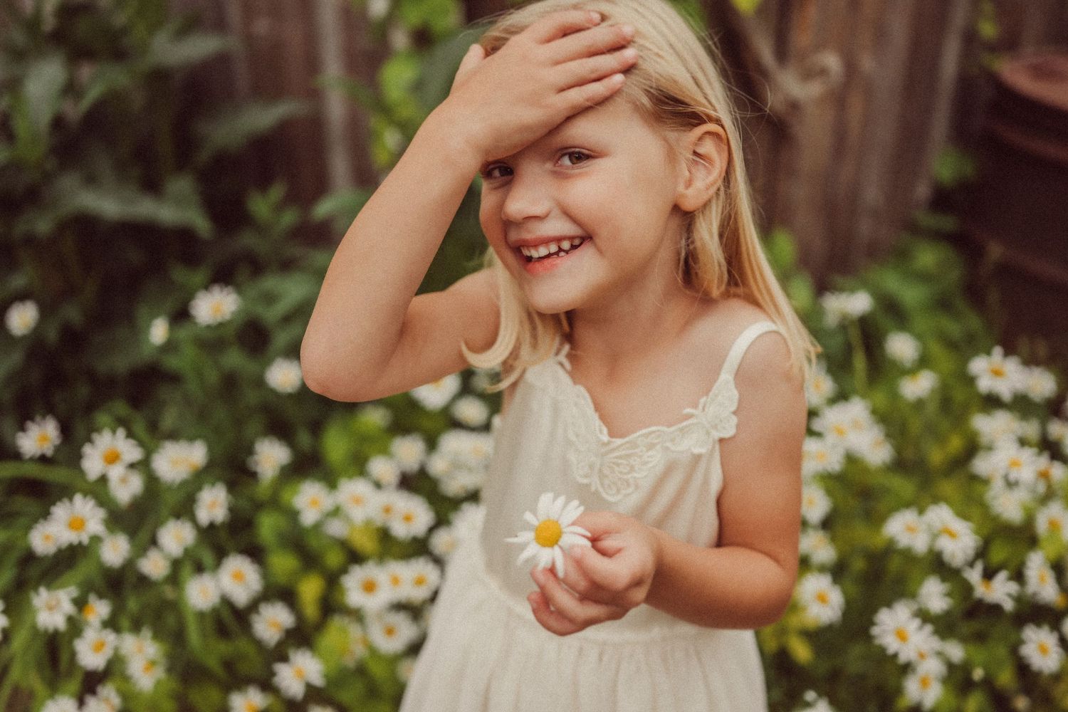 Playful summer portrait with child holding daisy in garden setting.