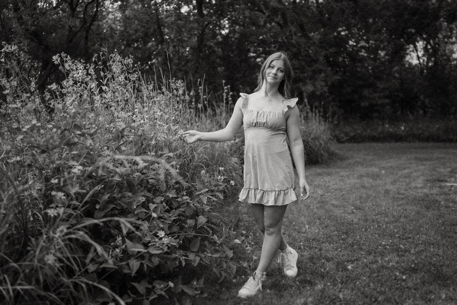 Black and white portrait in a garden setting featuring a ruffled dress and casual pose.
