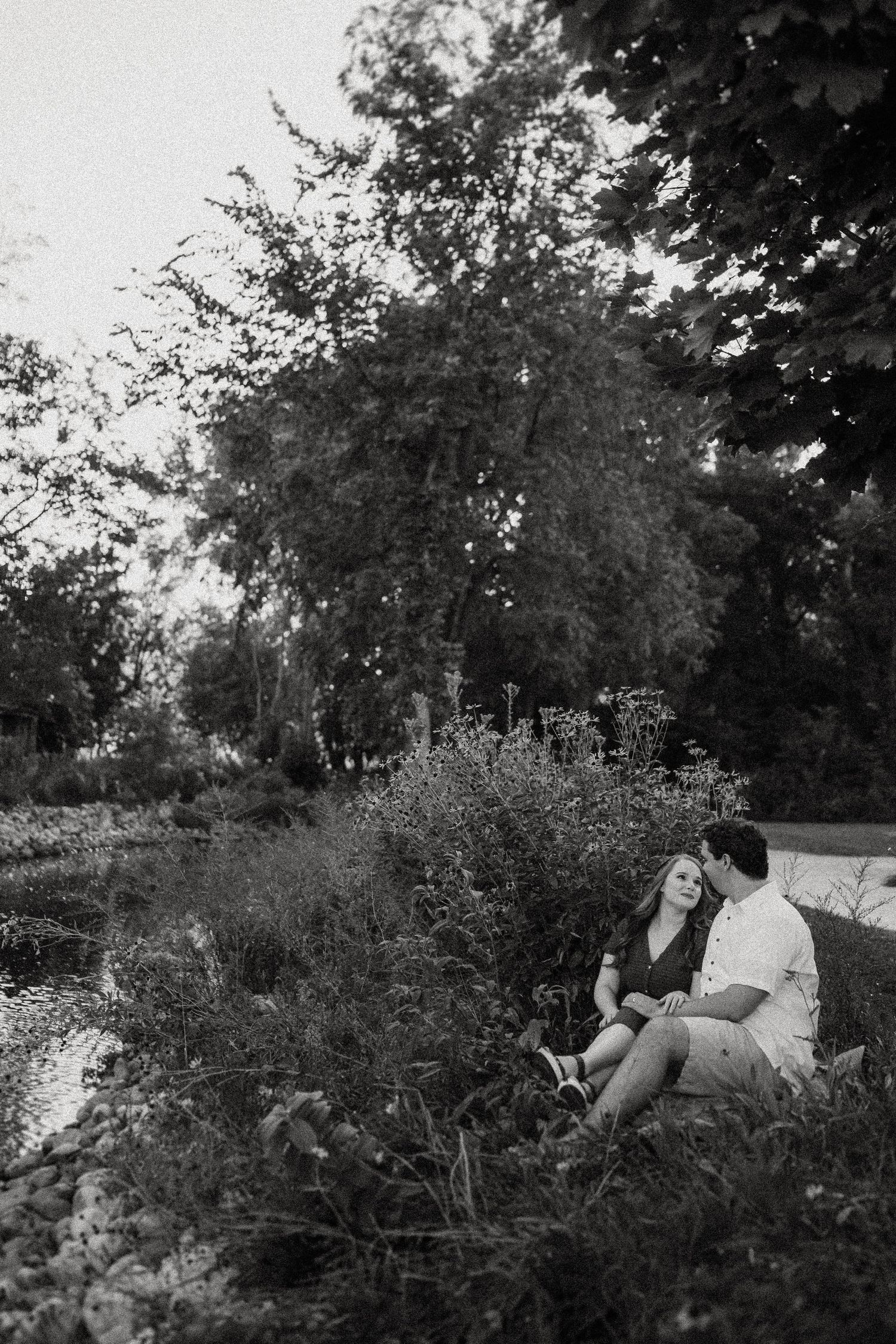 Couple sitting together by a pond in black and white photography.