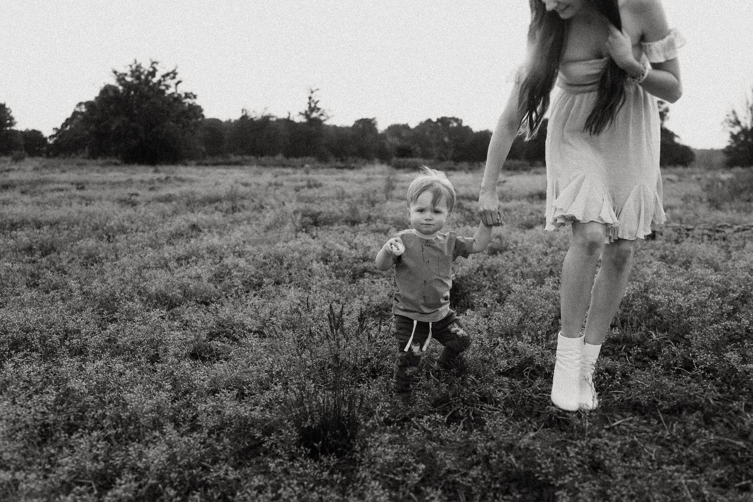 A black and white photo captures intimate family moments in a grassy field.