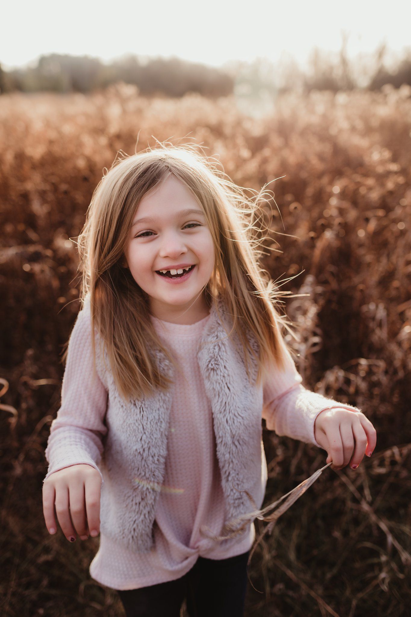 Young girl in pink sweater laughing joyfully in golden field.