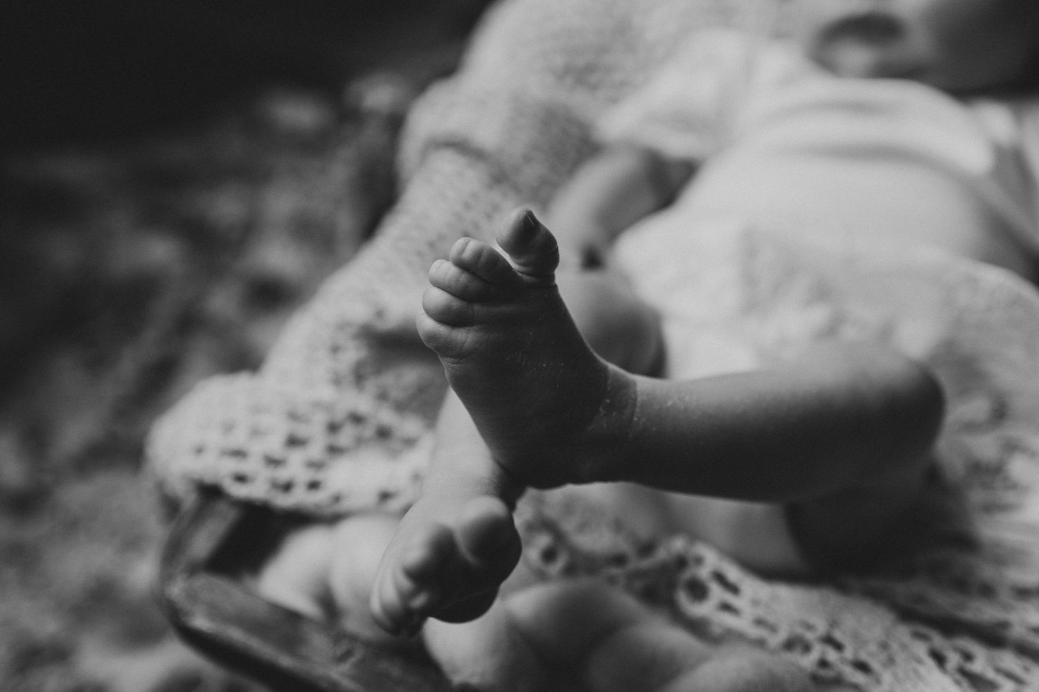 Black and white close-up of tiny baby feet resting on lacy fabric.