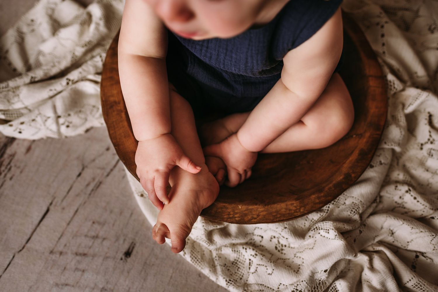 Close-up of tiny bare feet and legs sitting in wooden bowl on white lace fabric.