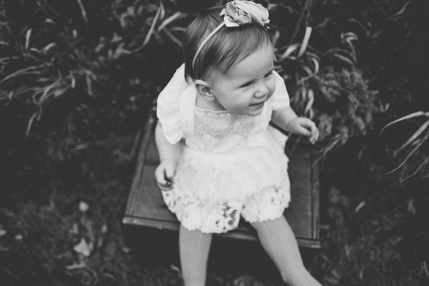 Black and white portrait of smiling baby in white lace dress.