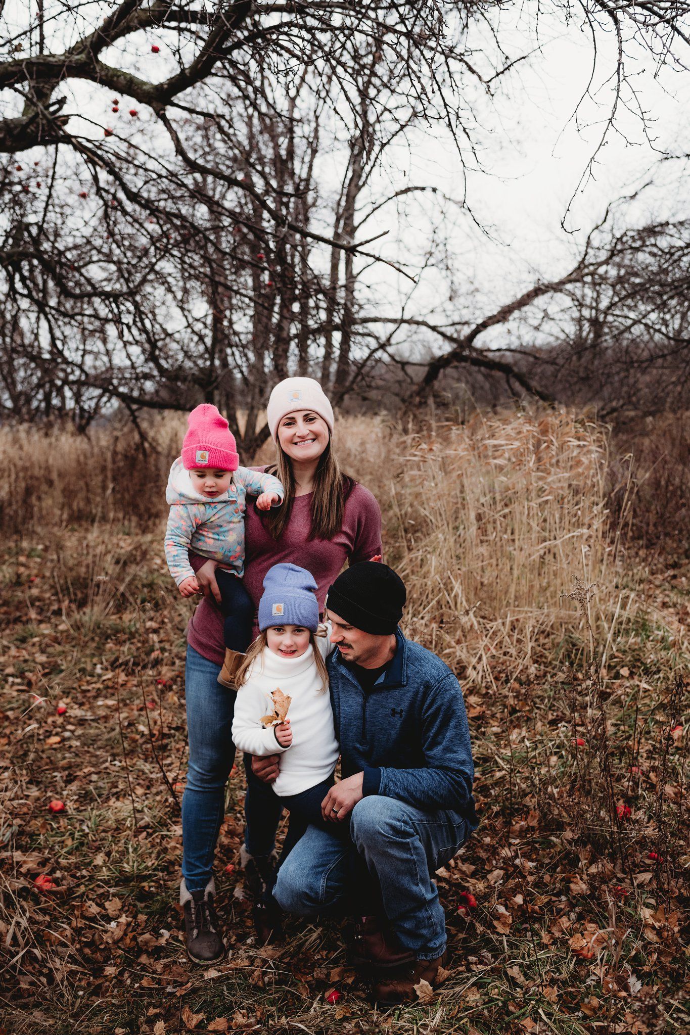 Autumn family portrait with warm clothing against backdrop of bare trees and fallen leaves.