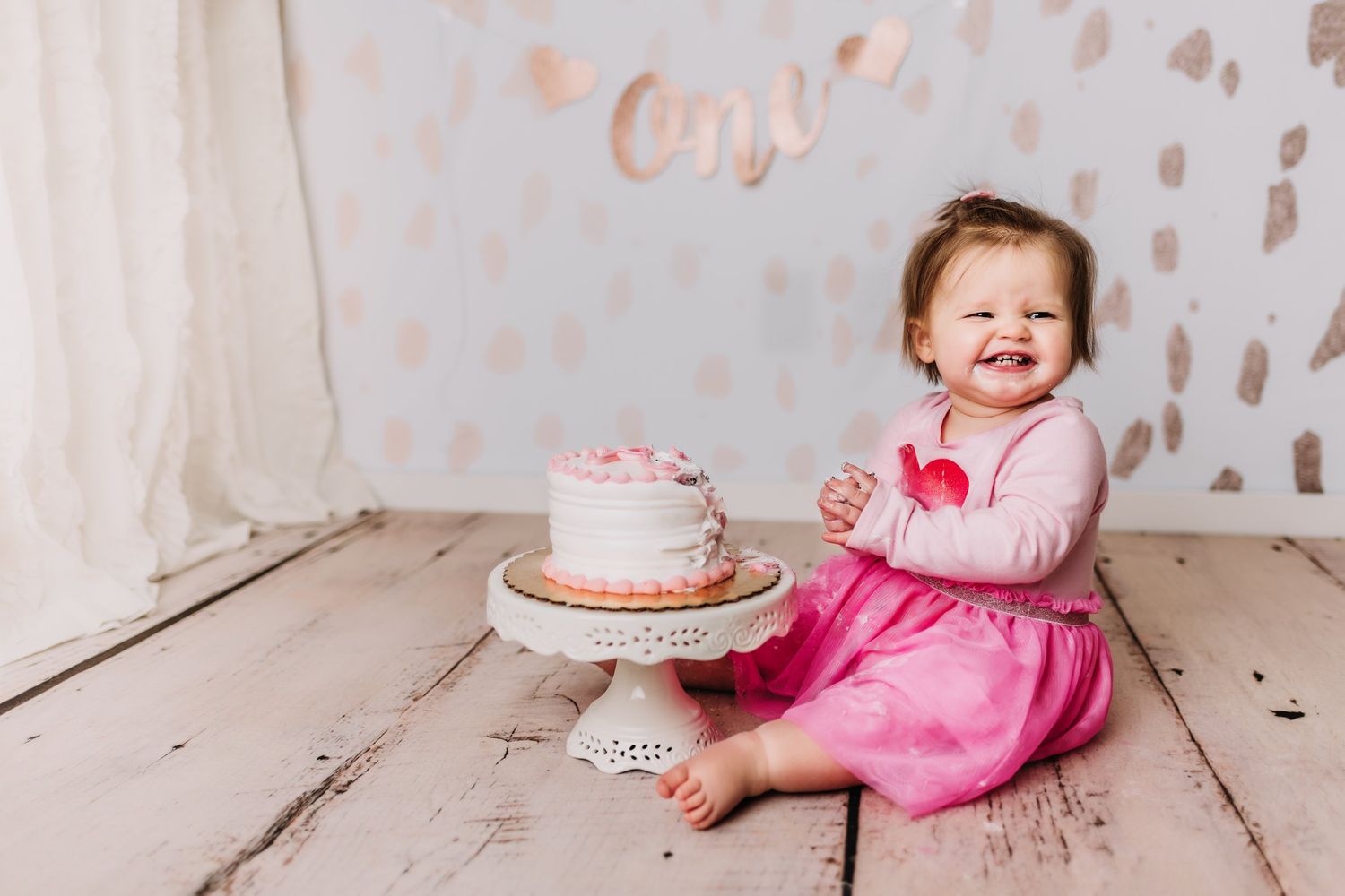 Joyful celebration moment with decorated cake on wooden floor against dotted backdrop.