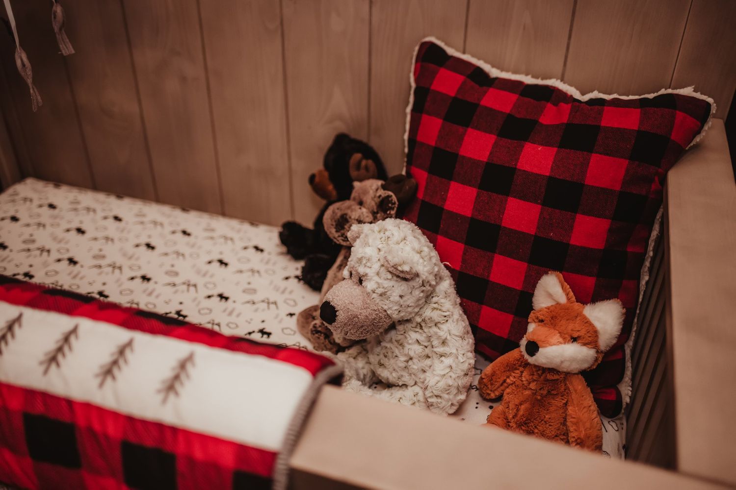 Cozy nursery corner with buffalo plaid pillows and stuffed woodland animal toys on display.