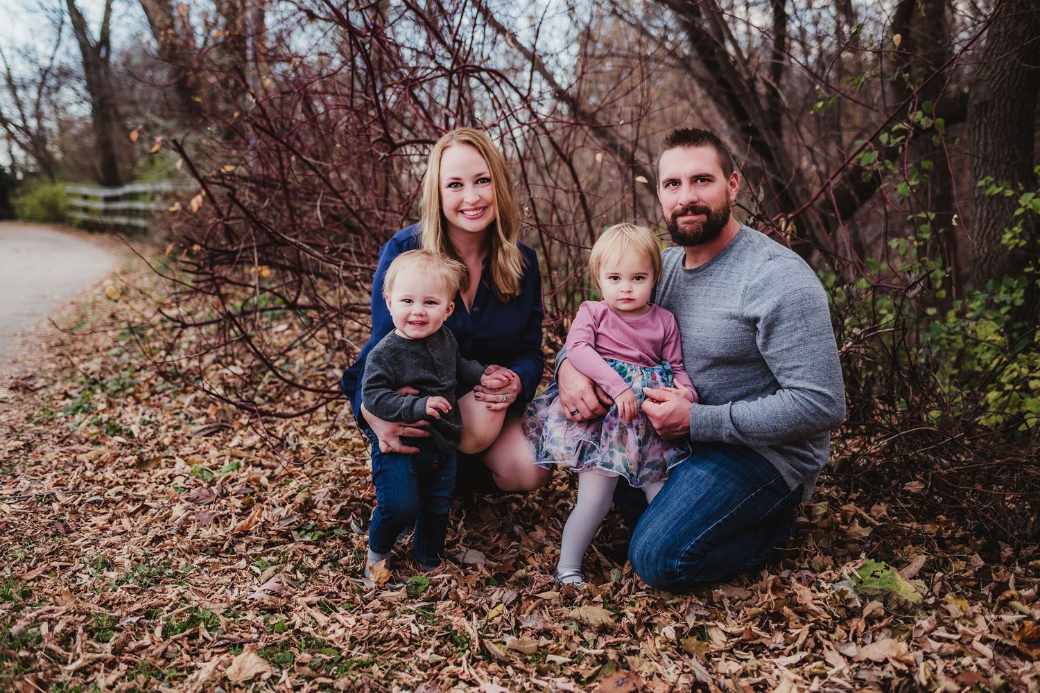 Family group kneeling together on path covered in fall leaves.