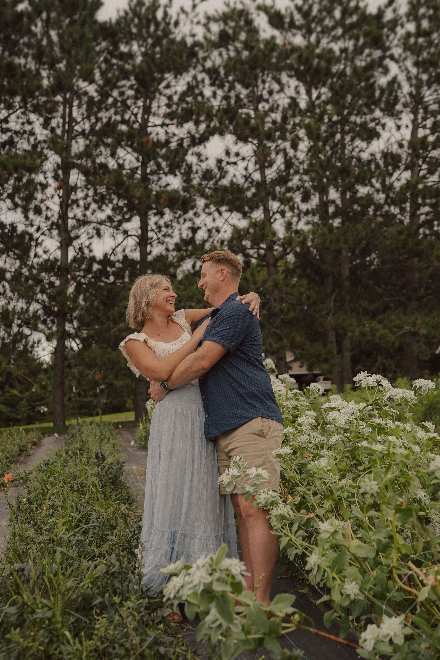A romantic moment captured in a lush garden surrounded by greenery and white flowers.