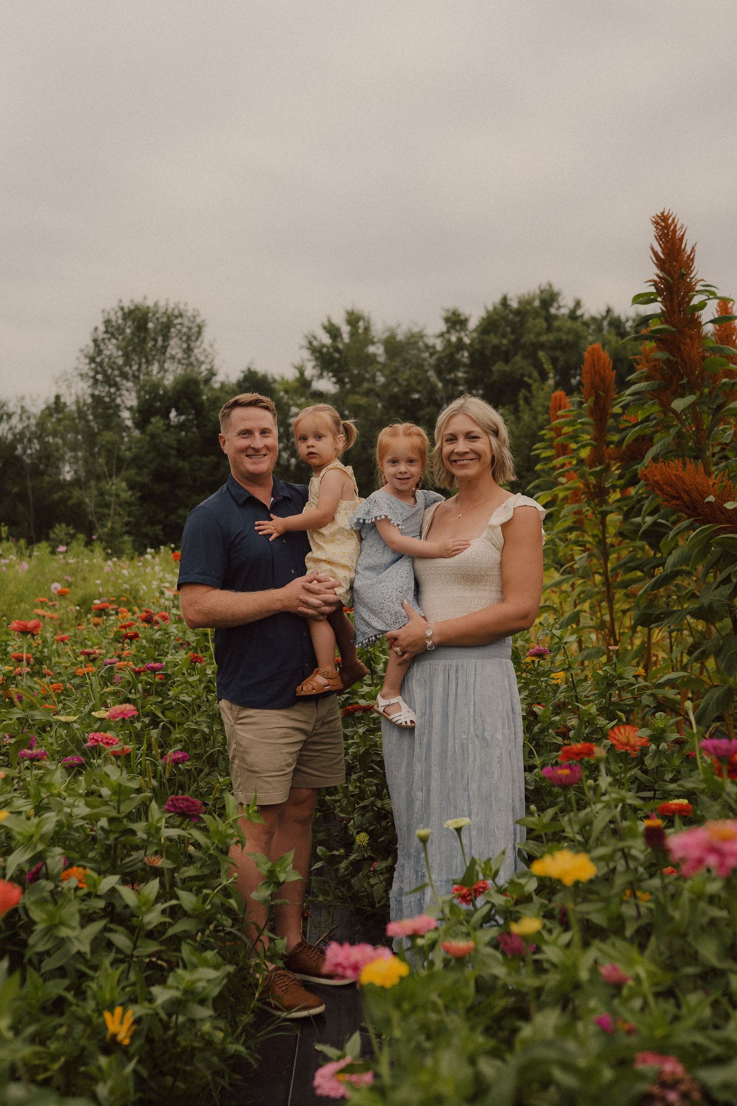 Family shares tender moments together while standing in a vibrant garden filled with colorful summer flowers and plants.