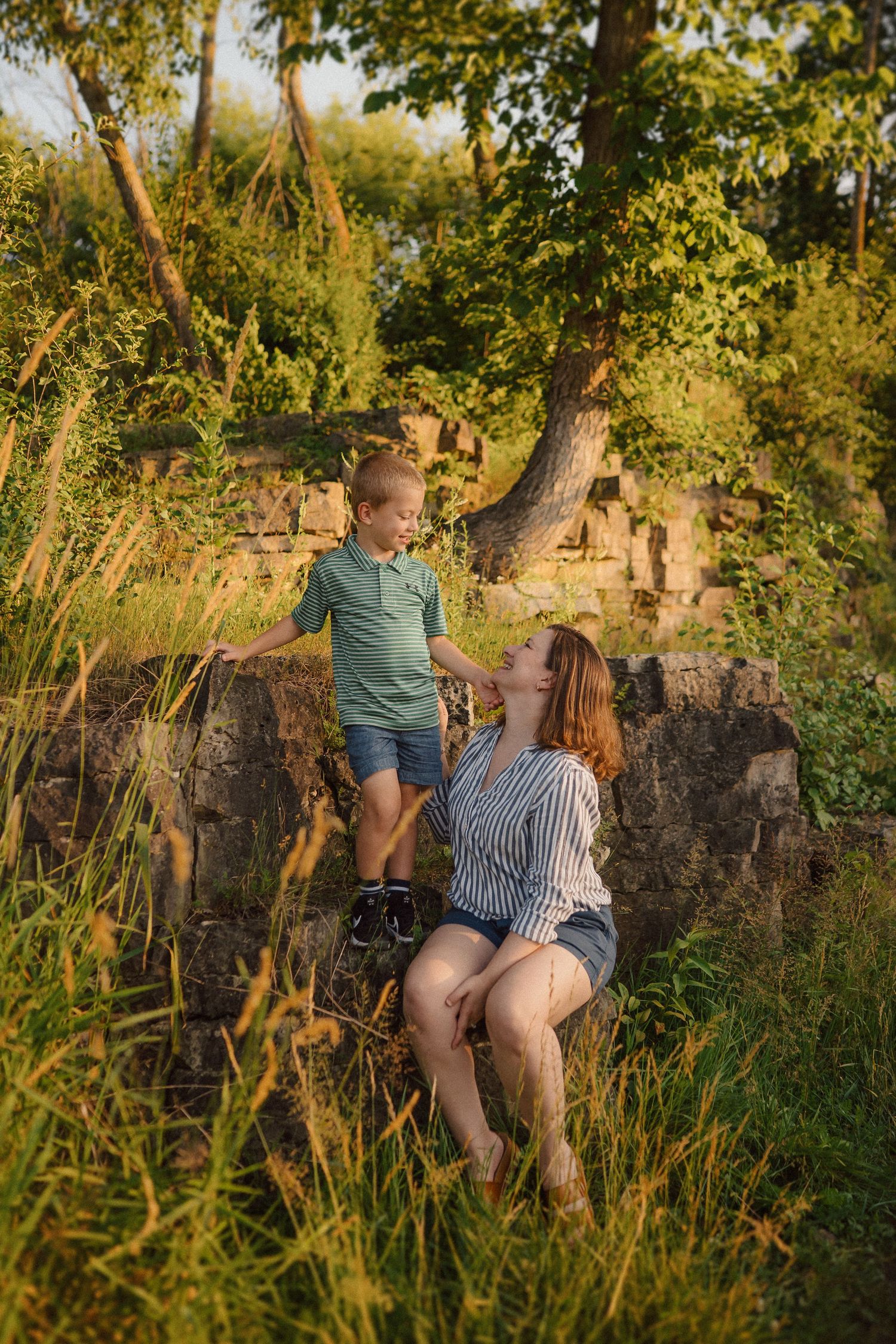 Family enjoying a golden sunset moment together in a lush natural setting beside a stone wall.