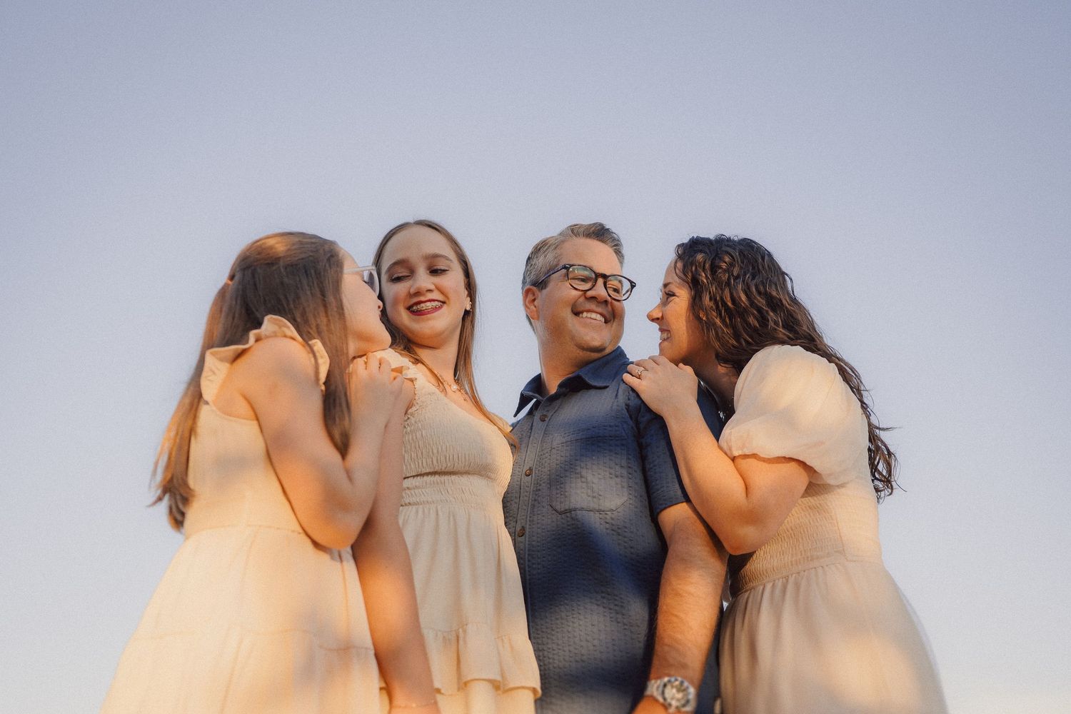 Group of people embracing and laughing together against a light blue sky background.