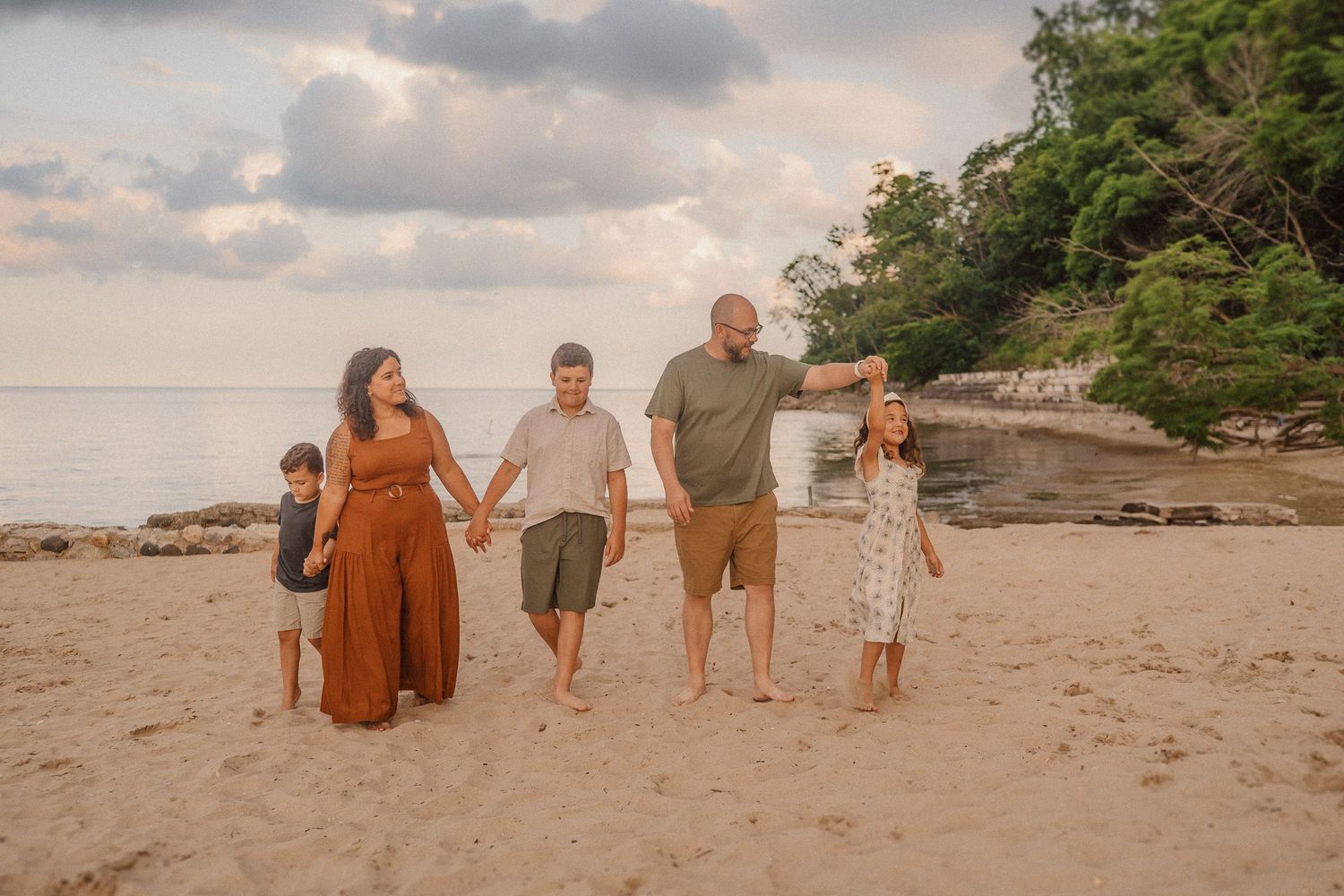 People enjoying a walk along a scenic sandy beach with trees and cloudy skies in the background.