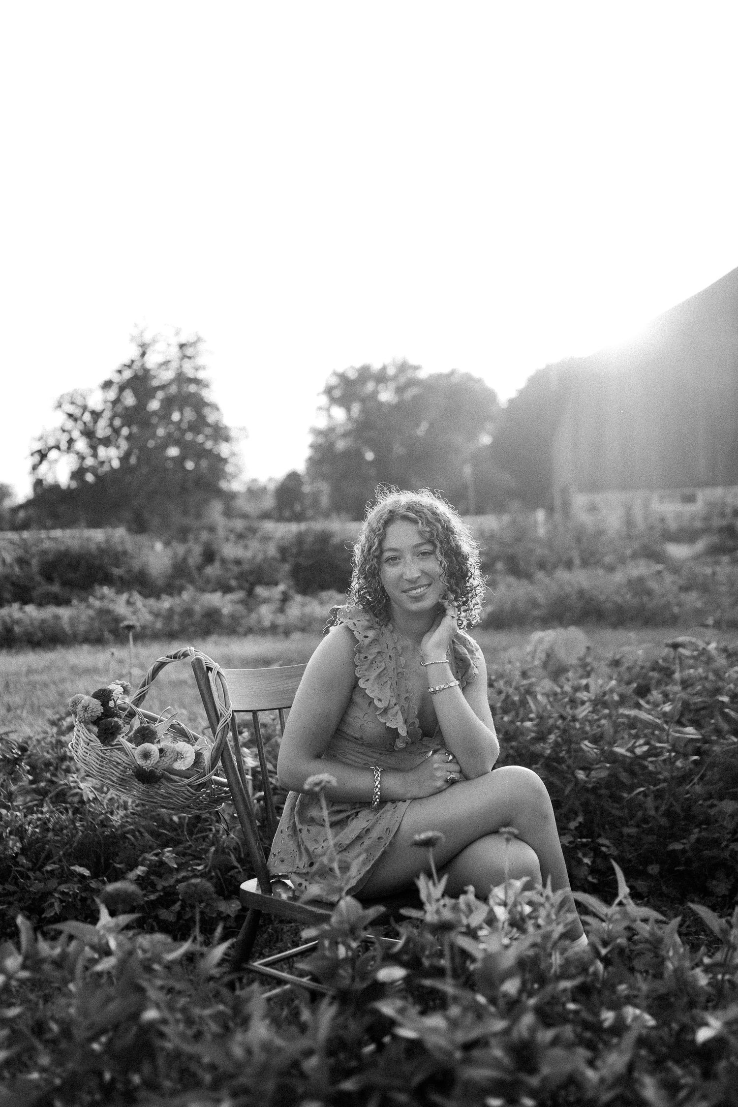 A person in a floral dress smiles joyfully while sitting in a lush garden on a sunny summer day.